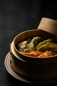 Fotografía gastronómica de gyozas en vaporera sobre fondo negro en Valencia.